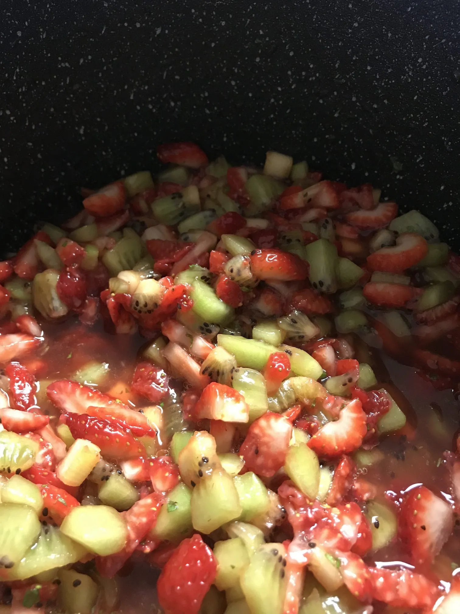 Closeup of strawberries and kiwis reducing in a pot